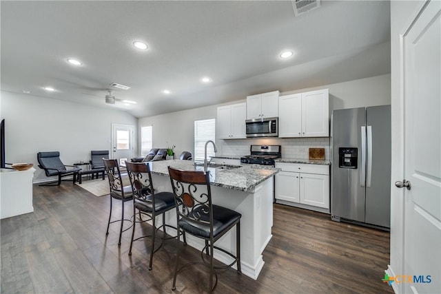 kitchen featuring tasteful backsplash, visible vents, appliances with stainless steel finishes, a sink, and a kitchen bar