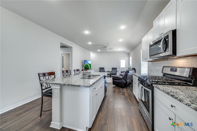 kitchen with stainless steel appliances, decorative backsplash, open floor plan, a sink, and a kitchen breakfast bar