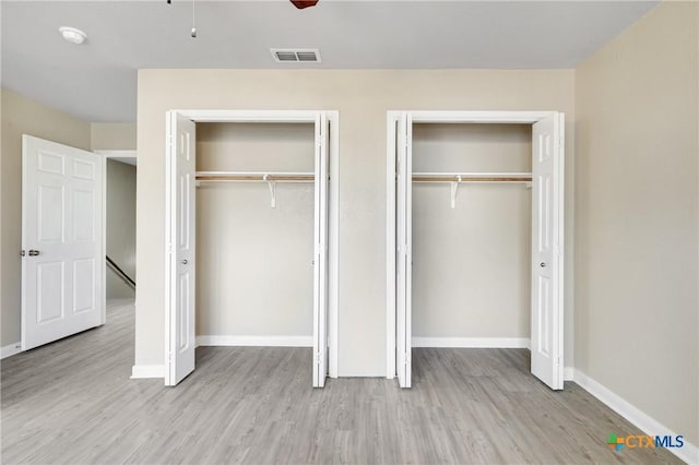 unfurnished bedroom featuring ceiling fan, two closets, and light wood-type flooring