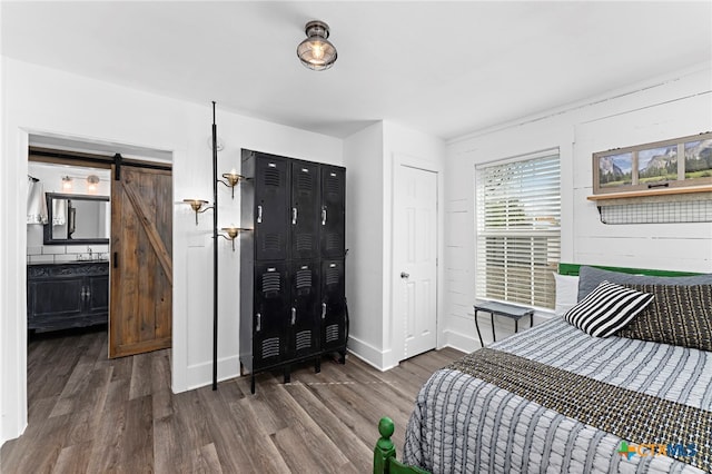 bedroom featuring ensuite bath, a barn door, dark hardwood / wood-style floors, and sink