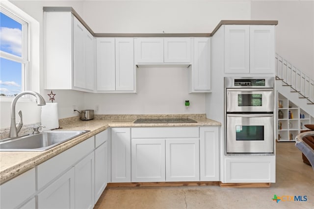 kitchen featuring black electric cooktop, stainless steel double oven, white cabinetry, and sink