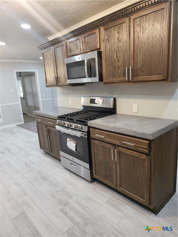 4106 Ermine Trl, Temple, TX 76504 - kitchen with appliances with stainless steel finishes, light wood-style floors, ornamental molding, recessed lighting, and dark brown cabinets
