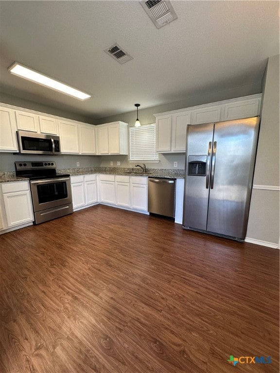 kitchen featuring stainless steel appliances, sink, hanging light fixtures, white cabinets, and dark wood-type flooring