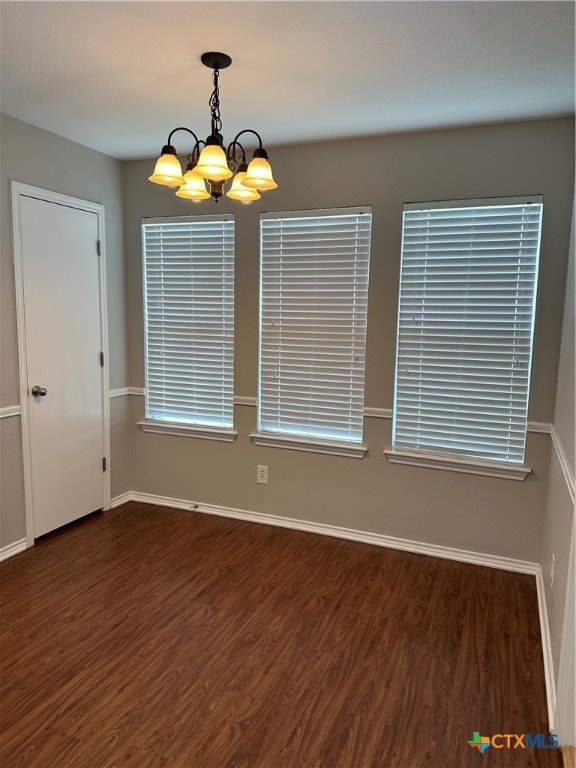 empty room with dark hardwood / wood-style floors and an inviting chandelier