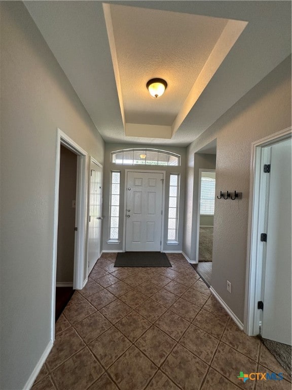 entryway featuring a textured ceiling, a raised ceiling, and dark tile patterned flooring