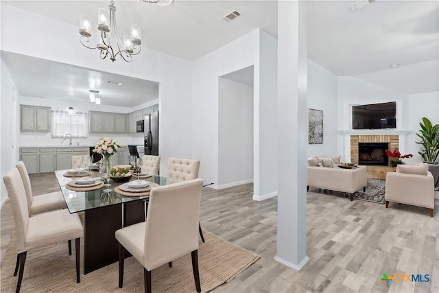 dining space with visible vents, a brick fireplace, light wood-style flooring, and an inviting chandelier