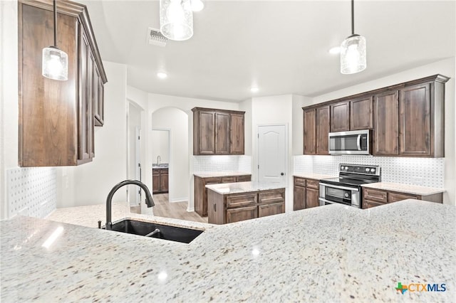 kitchen featuring sink, light stone countertops, hanging light fixtures, and appliances with stainless steel finishes