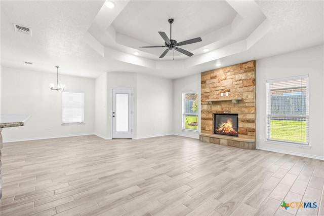 unfurnished living room with a fireplace, a raised ceiling, ceiling fan with notable chandelier, and light hardwood / wood-style flooring