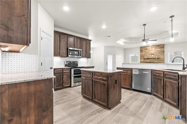 kitchen featuring dark brown cabinetry, light stone countertops, sink, a center island, and appliances with stainless steel finishes