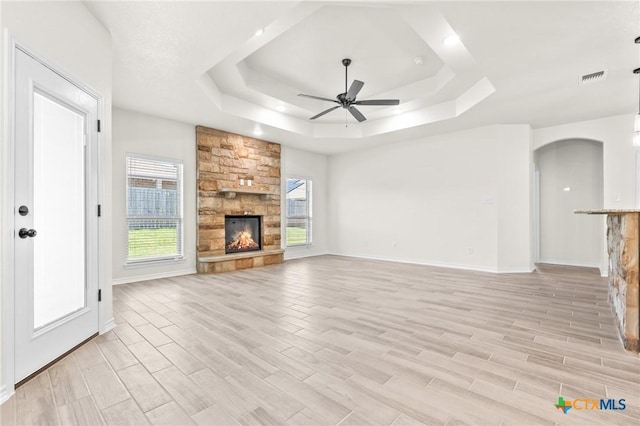 unfurnished living room with a fireplace, light hardwood / wood-style floors, a raised ceiling, and ceiling fan