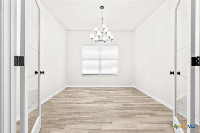 empty room featuring a notable chandelier and light wood-type flooring