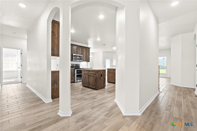 kitchen featuring appliances with stainless steel finishes, tasteful backsplash, dark brown cabinets, light hardwood / wood-style floors, and a kitchen island