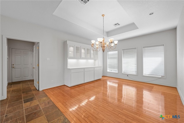 unfurnished dining area featuring dark hardwood / wood-style floors, a raised ceiling, and a notable chandelier