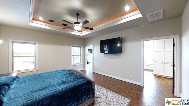 bedroom with ceiling fan, multiple windows, and a tray ceiling