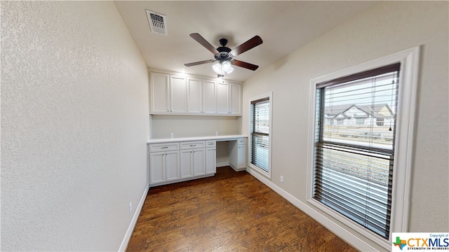 kitchen with a healthy amount of sunlight, dark wood-type flooring, built in desk, and white cabinets