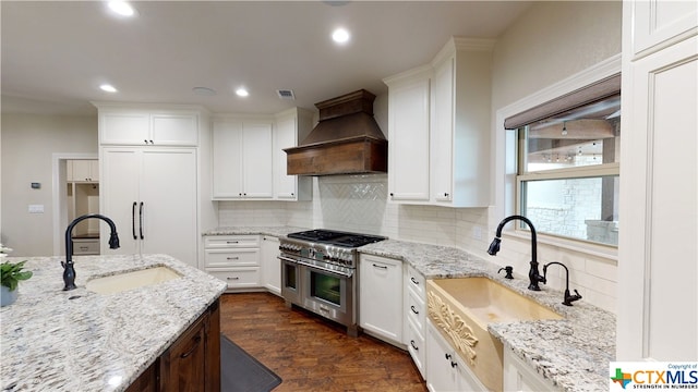 kitchen featuring high end appliances, custom range hood, sink, and white cabinets