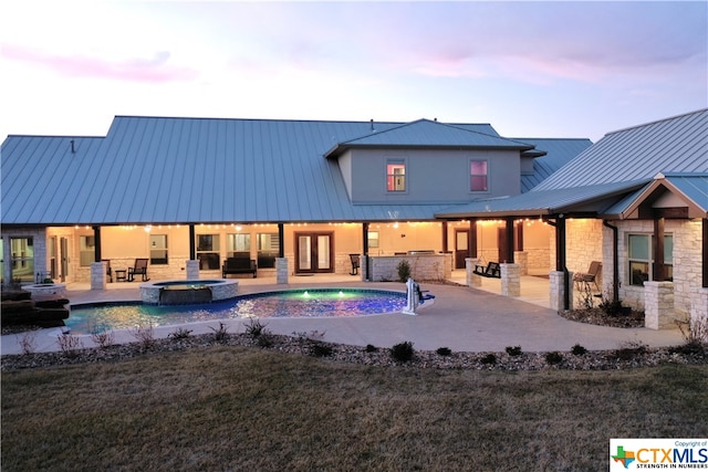 back house at dusk featuring a swimming pool with hot tub, a lawn, area for grilling, pool water feature, and a patio area