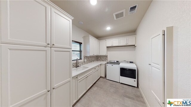 clothes washing area featuring cabinets, sink, and washing machine and clothes dryer