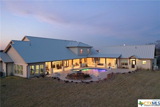 back house at dusk featuring a yard, a patio, and a pool with hot tub