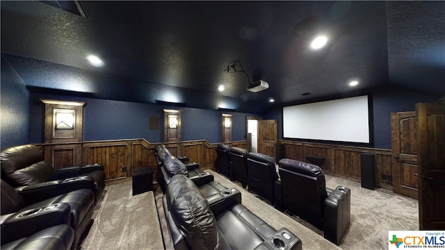 home theater with wood walls, light colored carpet, a textured ceiling, and vaulted ceiling