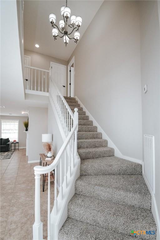 staircase featuring visible vents, baseboards, tile patterned flooring, a high ceiling, and a notable chandelier