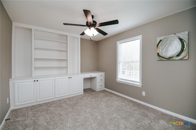 unfurnished office with baseboards, ceiling fan, built in shelves, and light colored carpet