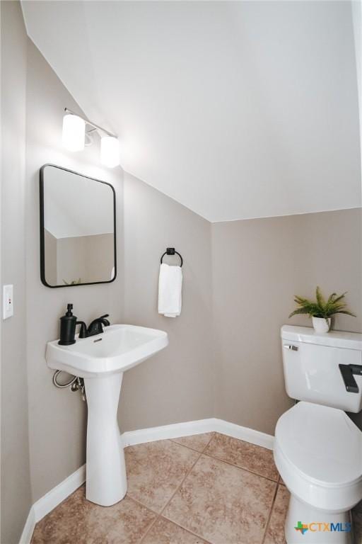 bathroom with toilet, vaulted ceiling, baseboards, and tile patterned floors