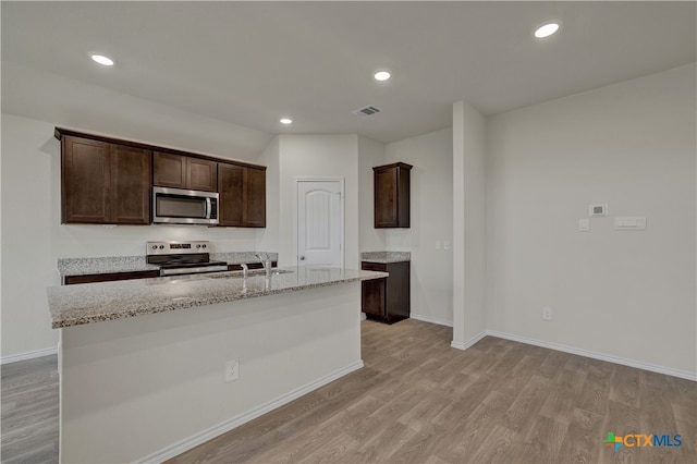 kitchen featuring light stone counters, stainless steel appliances, light wood-type flooring, dark brown cabinetry, and a kitchen island with sink