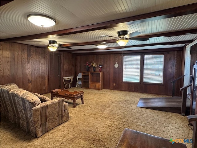 living room with beamed ceiling, ceiling fan, wood walls, and light carpet