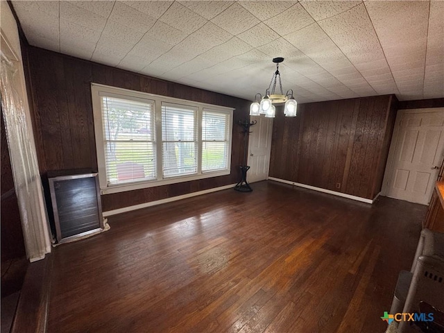 unfurnished dining area featuring wooden walls, dark hardwood / wood-style floors, and a notable chandelier