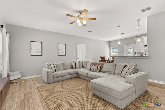 living room with baseboards, visible vents, light wood finished floors, and ceiling fan