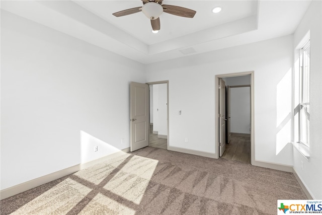 unfurnished bedroom with a walk in closet, a tray ceiling, ceiling fan, and light colored carpet