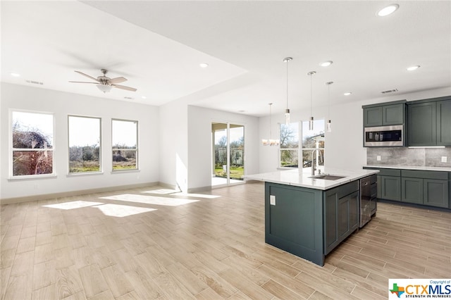 kitchen featuring sink, tasteful backsplash, pendant lighting, a center island with sink, and ceiling fan with notable chandelier