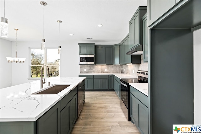 kitchen featuring light stone countertops, stainless steel appliances, a kitchen island with sink, sink, and decorative light fixtures