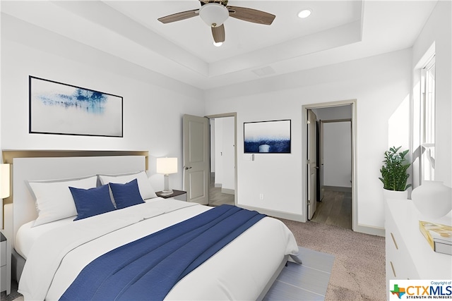 bedroom featuring light carpet, connected bathroom, a raised ceiling, and ceiling fan