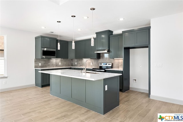 kitchen with pendant lighting, sink, light stone countertops, an island with sink, and stainless steel appliances