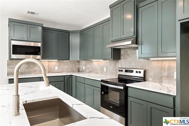 kitchen featuring light stone countertops, sink, stainless steel appliances, and green cabinetry