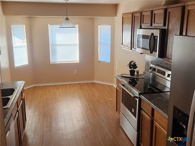 kitchen with light wood-type flooring, stainless steel appliances, decorative light fixtures, sink, and dark stone countertops