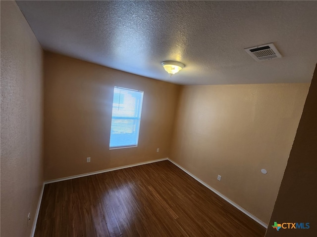 empty room with dark hardwood / wood-style flooring and a textured ceiling