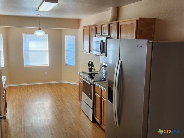 kitchen with a textured ceiling, hanging light fixtures, stainless steel appliances, and light hardwood / wood-style flooring