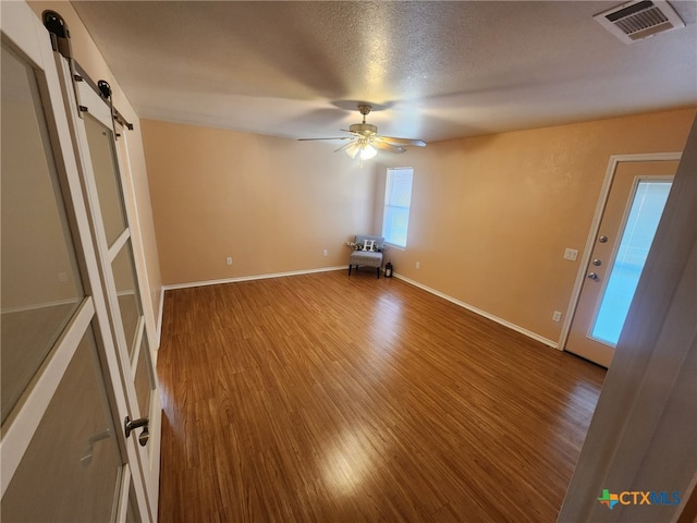 spare room with hardwood / wood-style flooring, ceiling fan, a barn door, and a textured ceiling