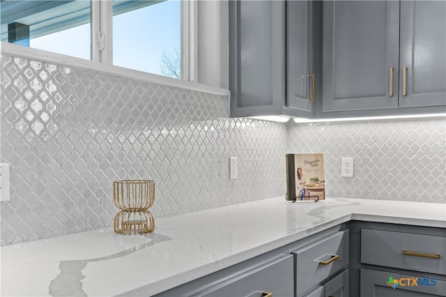 kitchen featuring decorative backsplash, light stone counters, and gray cabinetry