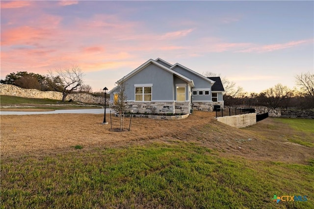 view of front facade with stone siding, a water view, a yard, and stucco siding