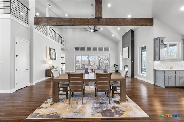 dining space with beam ceiling, dark wood finished floors, a glass covered fireplace, high vaulted ceiling, and baseboards