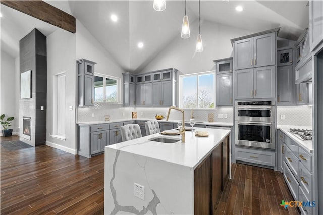 kitchen with dark wood-style flooring, a fireplace, gray cabinetry, appliances with stainless steel finishes, and an island with sink