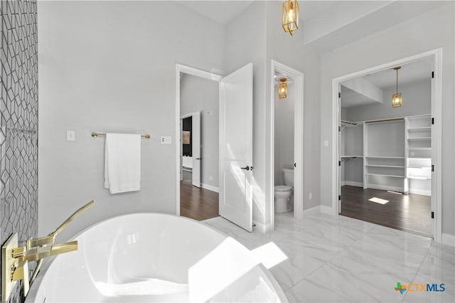 full bathroom featuring toilet, marble finish floor, baseboards, and a soaking tub