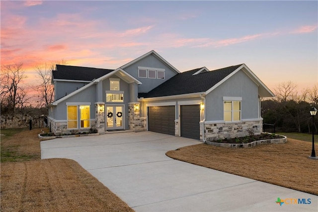 craftsman inspired home with french doors, stucco siding, a garage, stone siding, and driveway