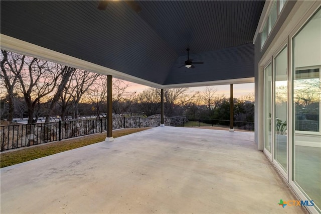 patio terrace at dusk featuring ceiling fan and fence