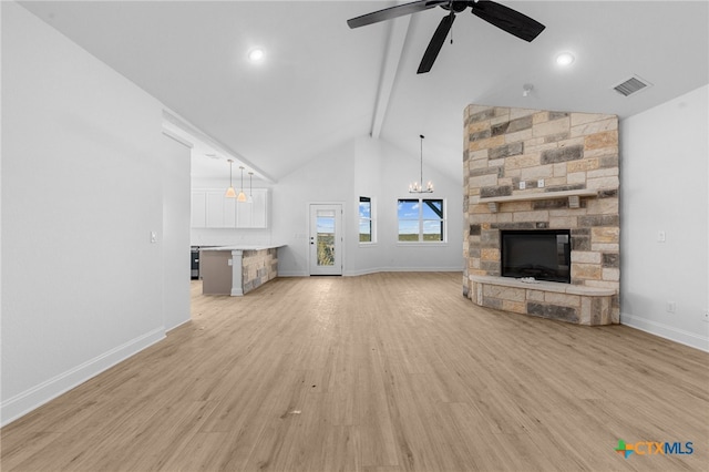 unfurnished living room featuring a stone fireplace, ceiling fan with notable chandelier, high vaulted ceiling, beam ceiling, and light wood-type flooring