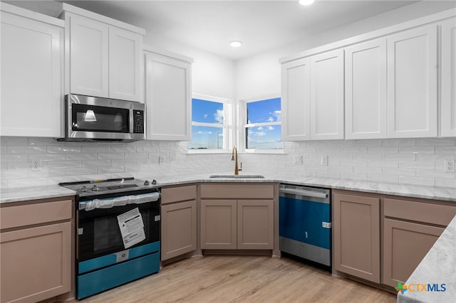 kitchen with white cabinetry, appliances with stainless steel finishes, decorative backsplash, sink, and light hardwood / wood-style flooring